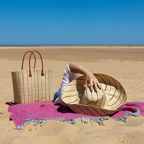 Large Mimosa Hat and Large Hanta Pinstripe Tote Bag in a natural pinstripe design worn by lady on a beach in the sunshine