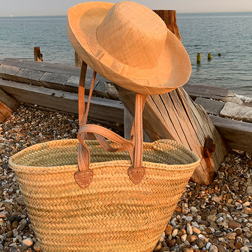 Mimosa raffia Hat in natural with a small double handle palm leaf basket at the seaside