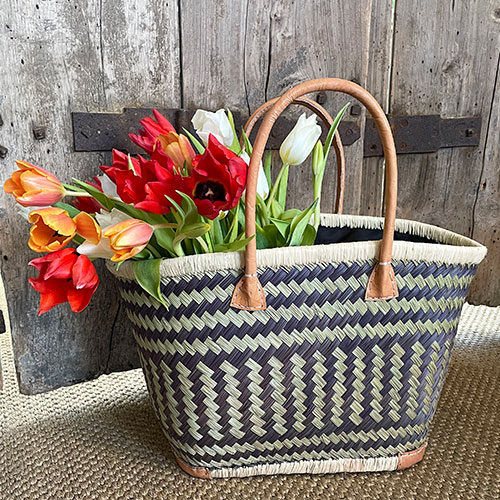 Small drawstring shopping bag in black and natural grass and raffia with a bunch of tulips beside French shutters
